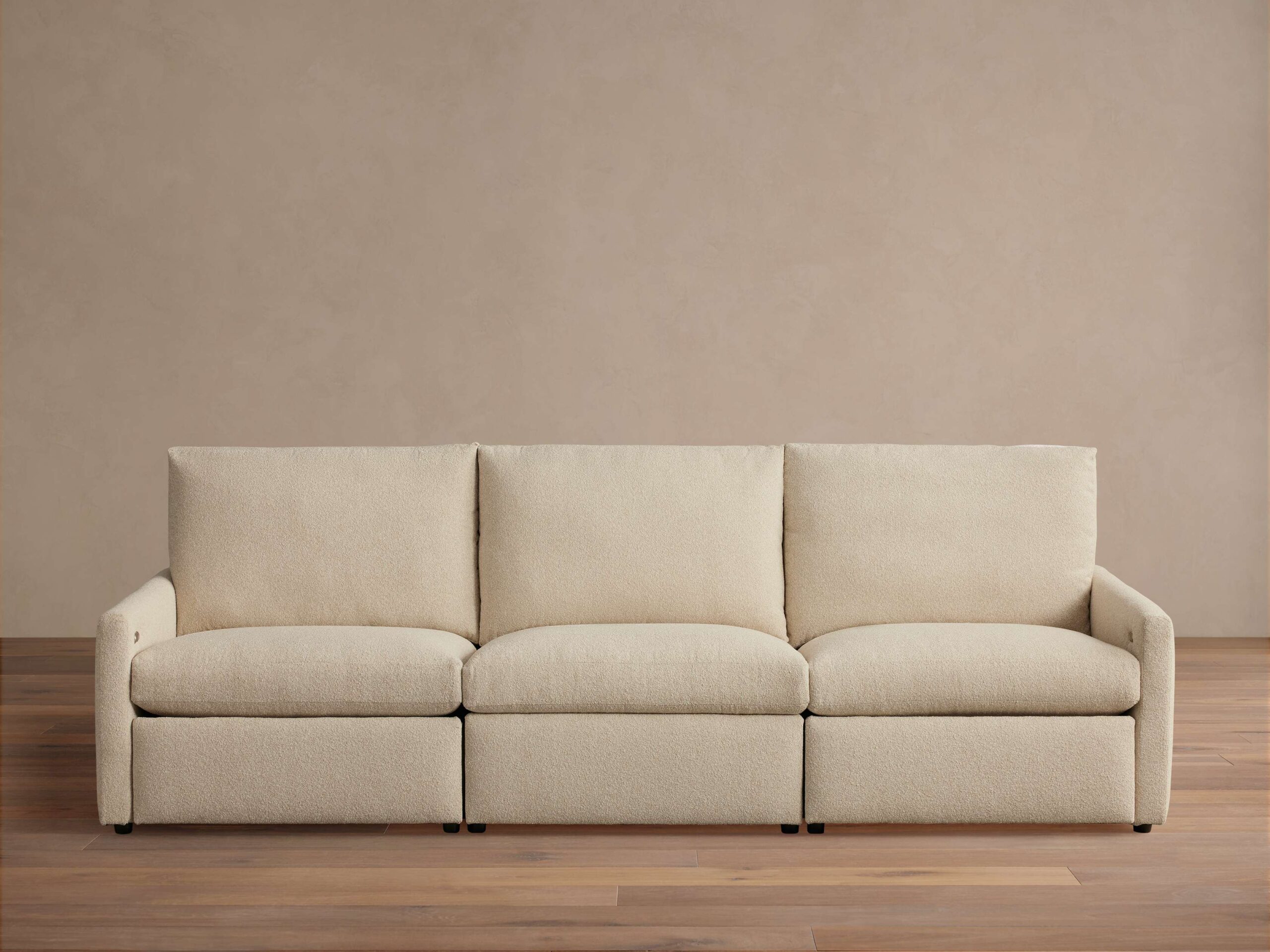 Kipton Three-Piece Motion Modular Sofa in beige fabric, shown in a simple, modern room. Three cushioned seats and slim arms.