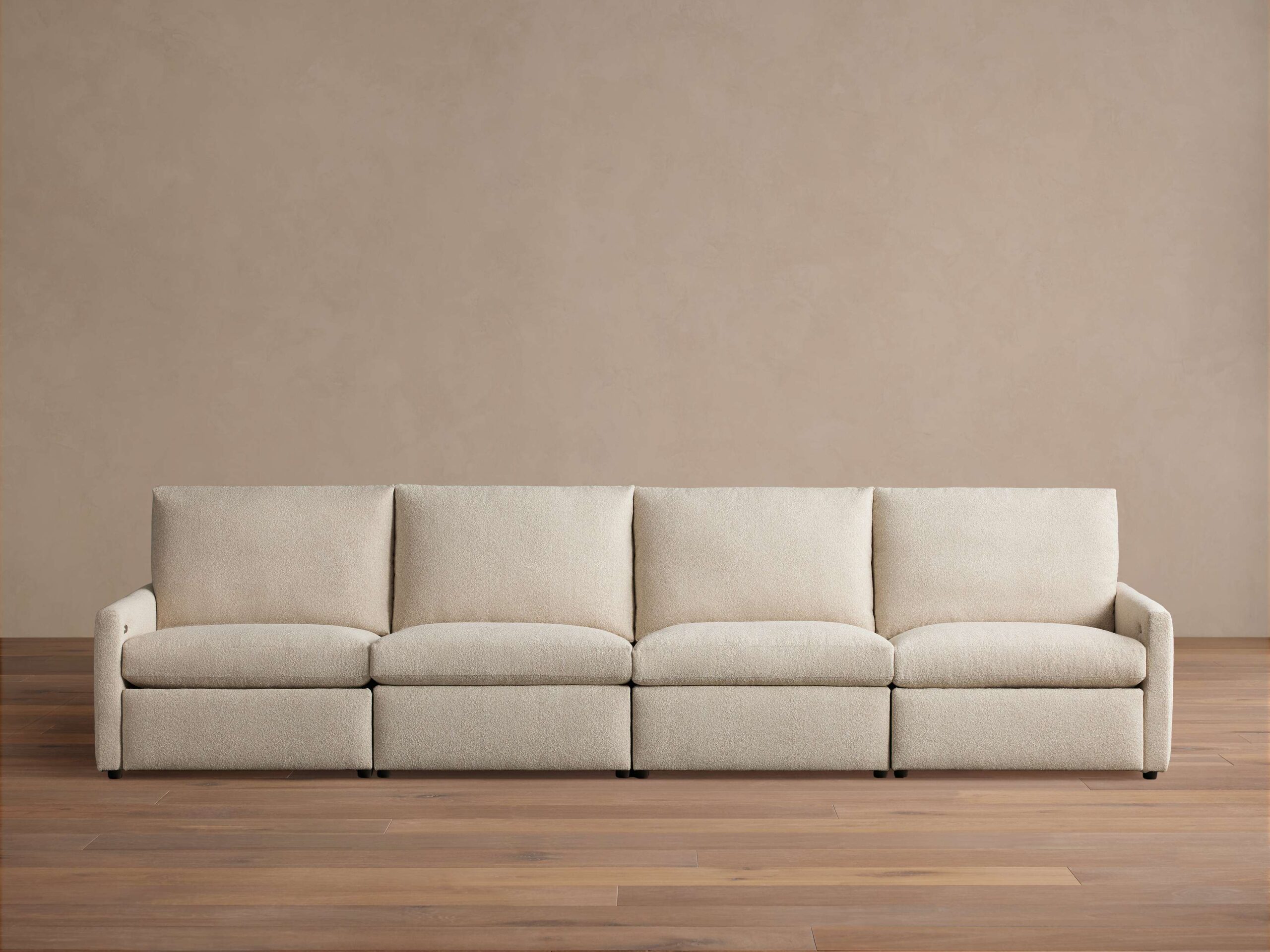 Kipton Four-Piece Motion Modular Sofa in beige fabric, viewed from the front. Features slim arms, four cushioned seats, and backrests, on a wooden floor.