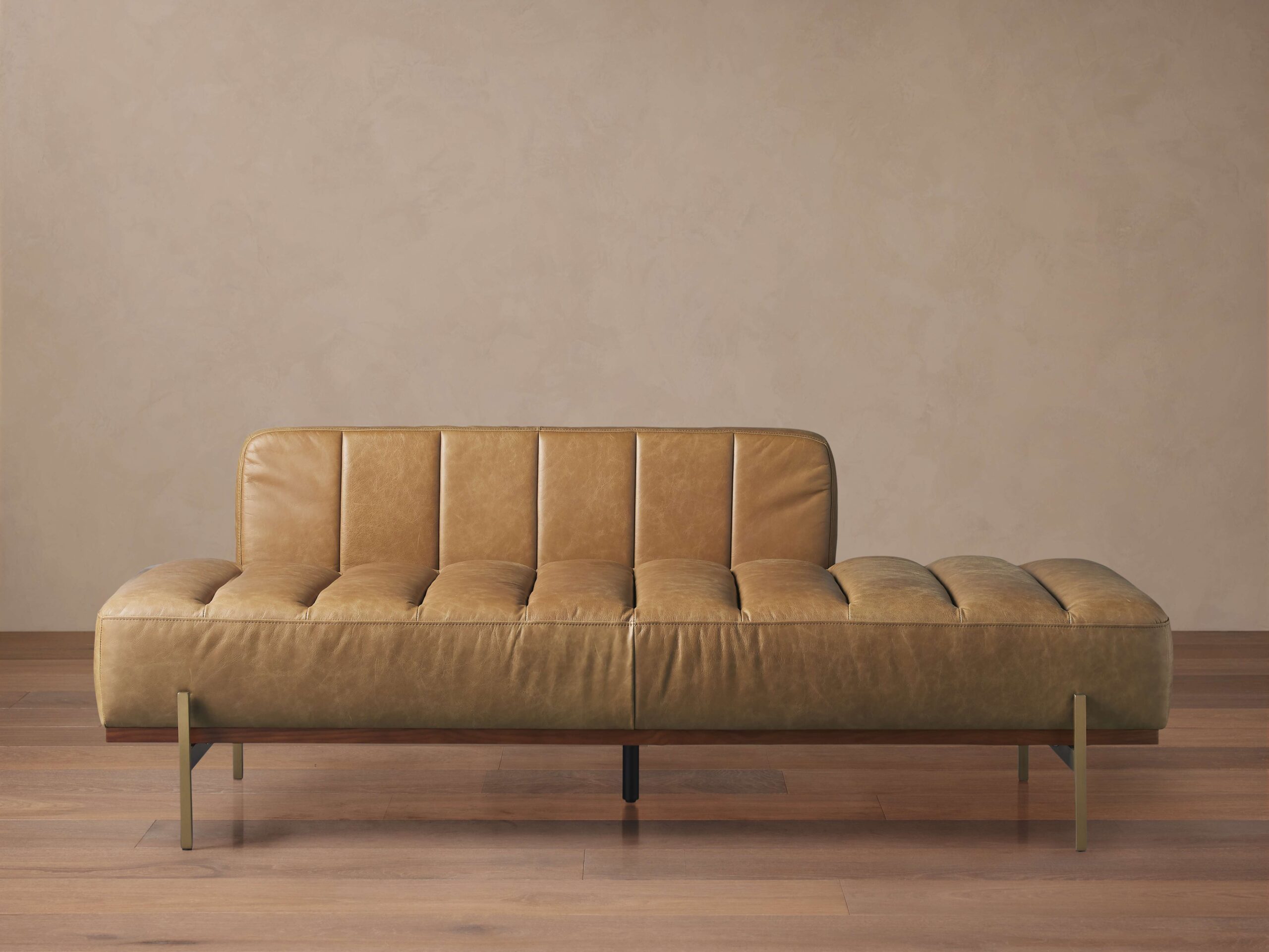 Lansing Leather Daybed in caramel brown top grain leather, featuring vertical stitching, low backrest, and metal legs, on wooden floor.