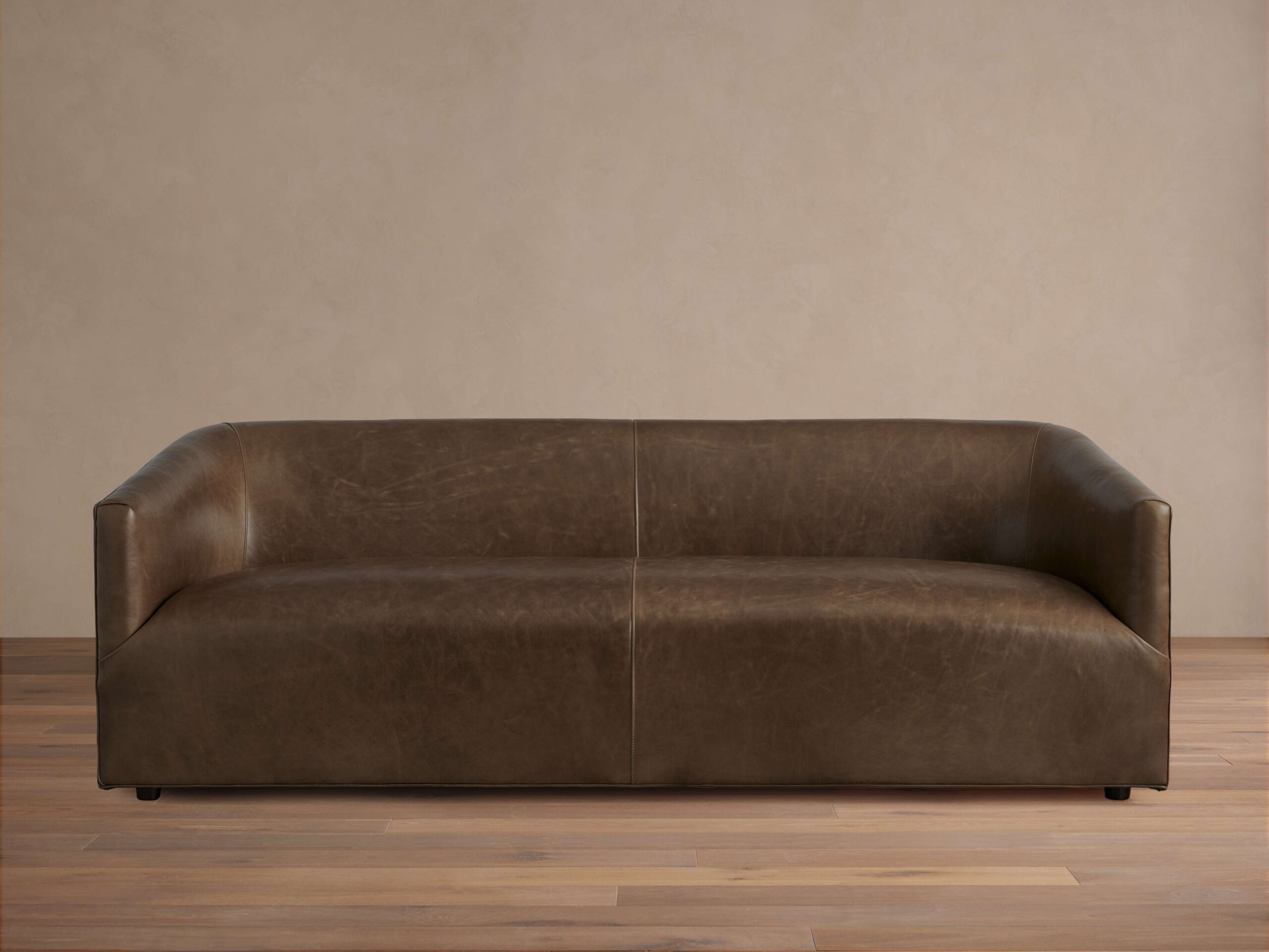 Brown Ellison Leather Sofa with a sleek, modern design. Features smooth, continuous curves and a slight sheen, set on a wooden floor.